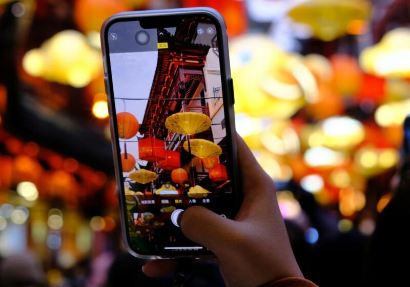Hand holding mobile phone taking photo of lanterns